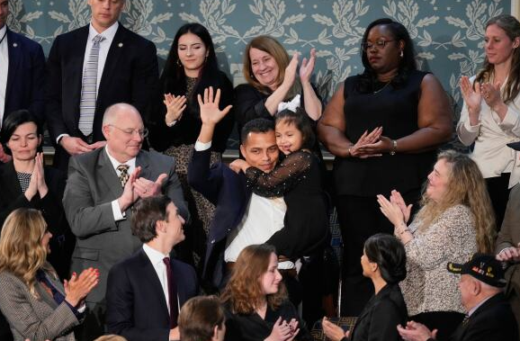 Diverse crowd applauds as a couple in the center raises their hands in celebration, embracing each other.