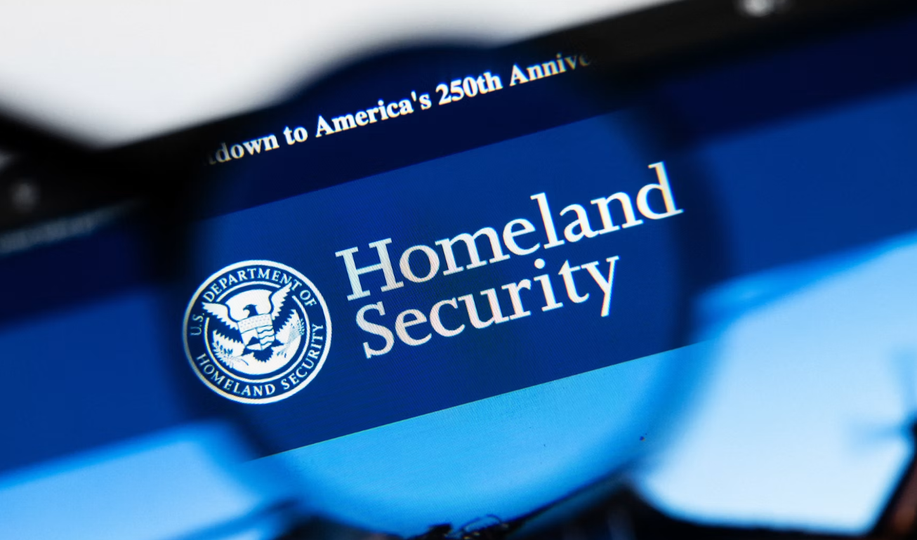 Close-up of a computer screen showing the U.S. Department of Homeland Security logo and the words 'Homeland Security' on a blue background, with a magnifying glass blur in the foreground.