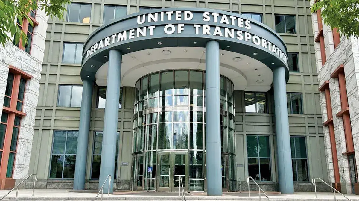 Front entrance of the United States Department of Transportation building with a curved glass rotunda and blue pillars.