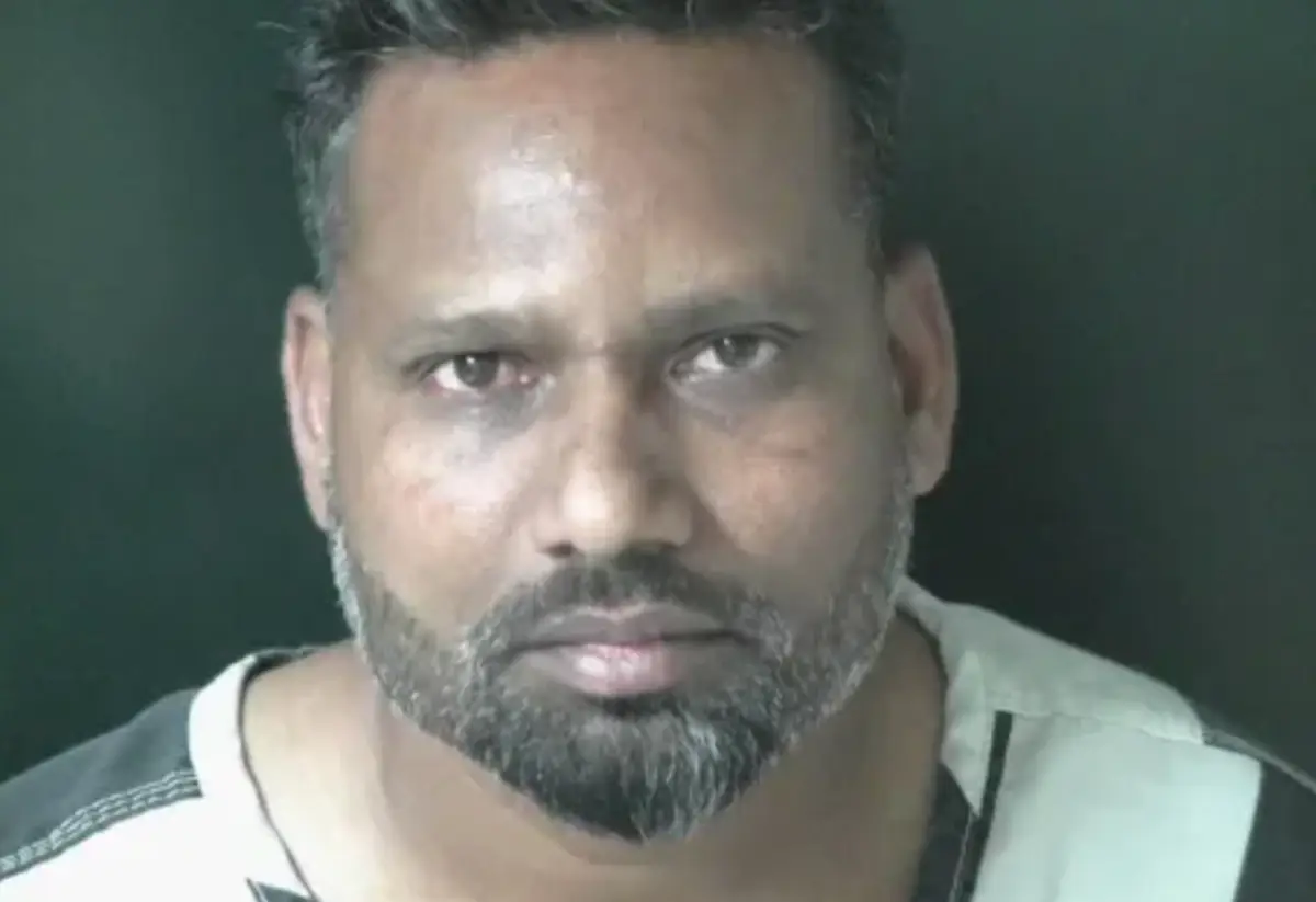 Close-up portrait of a man with a dark beard and short hair, looking at the camera against a dark green background.