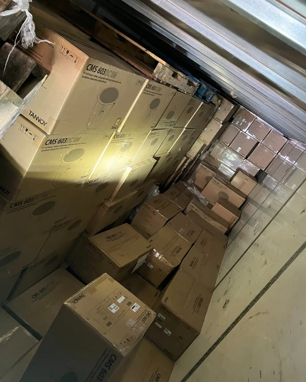 A narrow storage corridor filled with stacked cardboard boxes labeled CMS 603 on a loading dock or truck interior at an angle.