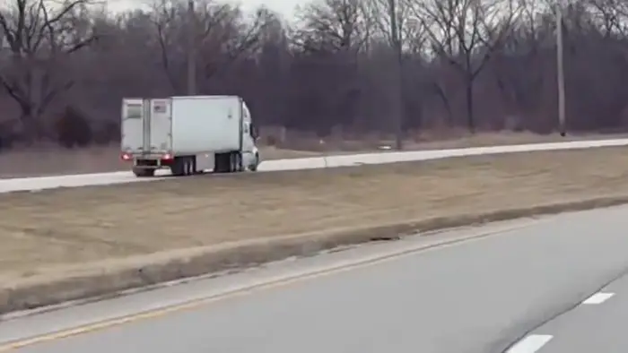 White box truck parked on the highway shoulder with bare trees in the background.
