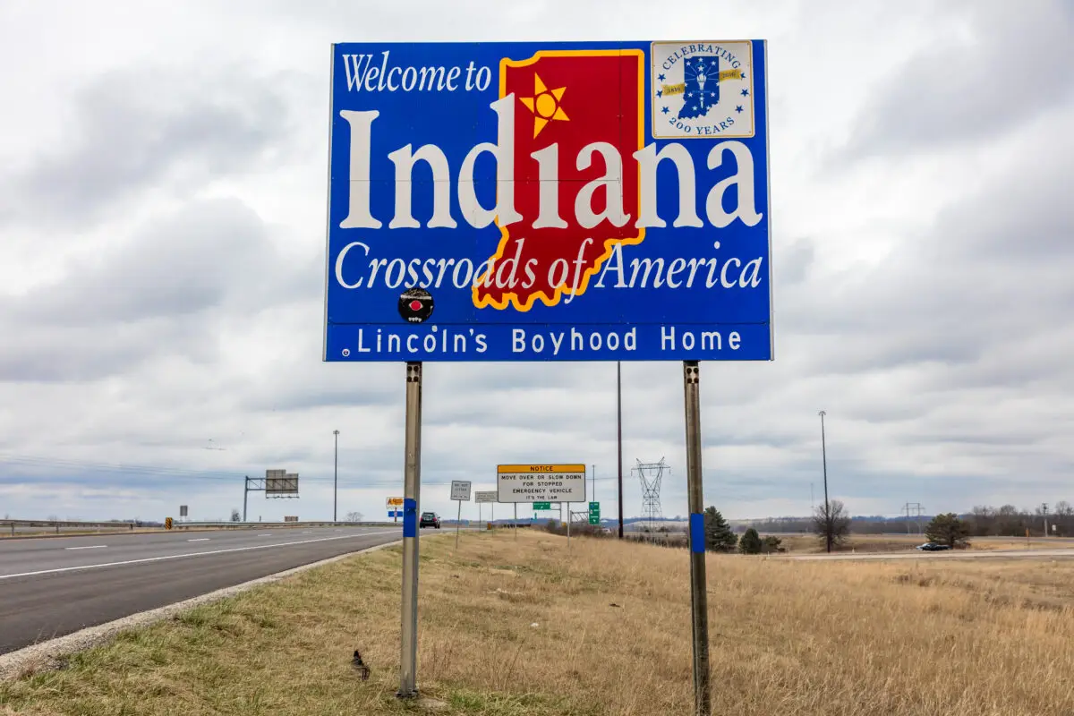 Large blue 'Welcome to Indiana' sign beside a highway, with 'Crossroads of America' and 'Lincoln's Boyhood Home' text