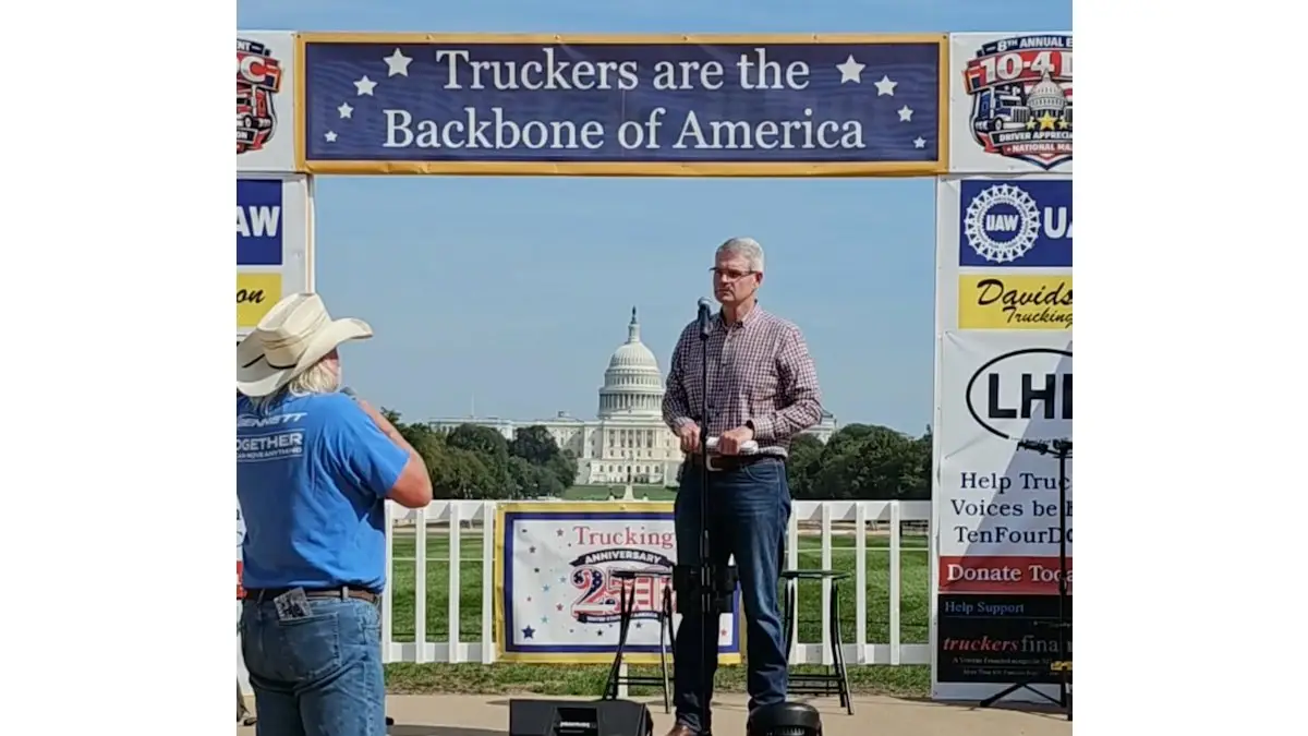 Man speaking at a microphone in front of the U.S. Capitol, with a truckers event banner.